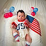 baby, infant, flag, american_flag, balloons, patriotic, white_background, cushion, clothing, socks, person, indoor, celebration, cute, portrait, newborn, holiday, festive, red, blue