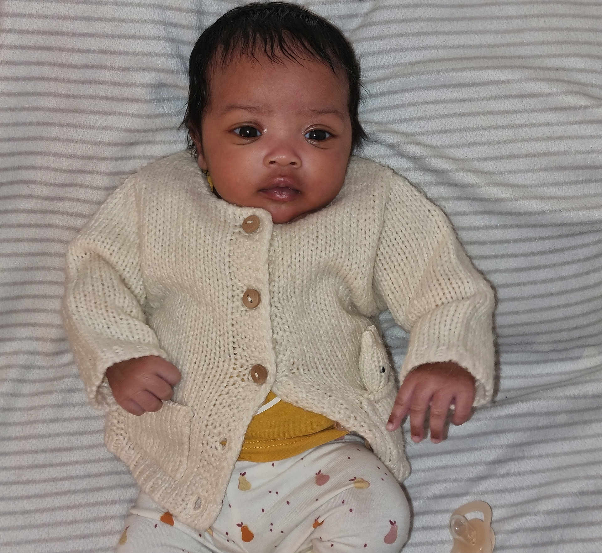 Tia a rejoint le concours — aidez-le/la à gagner de superbes lots ! baby, infant, knitwear, sweater, blanket, striped, clothing, face, hand, lying_down, cute, child, person, indoors, pacifier, patterned_pants, soft_texture, portrait, young, warm