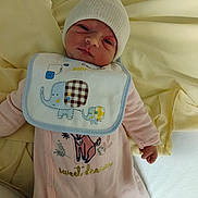 Léonie a rejoint le concours — aidez-le/la à gagner de superbes lots ! baby, newborn, infant, onesie, bib, hat, blanket, soft, cute, lying_down, pink_clothing, white_hat, elephant_design, indoors, child, face, portrait, sleepwear, hand, cozy