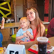 Joslyn is registered to the contest to win money with this photo: child, toddler, restaurant, fast_food, table, drink, smile, happy, blond_hair, long_hair, clothing, food, cup, number, indoor, person, family, casual, seated, portrait