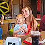 child, toddler, restaurant, fast_food, table, drink, smile, happy, blond_hair, long_hair, clothing, food, cup, number, indoor, person, family, casual, seated, portrait