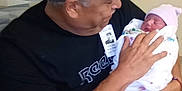 Miracle Maya joined the competition — help win amazing prizes! man, baby, newborn, hospital, cap, shirt, shorts, glasses, chair, blanket, person, indoor, holding, seated, tenderness, family, love, portrait, smile, hat