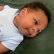 Melyo a rejoint le concours — aidez-le/la à gagner de superbes lots ! baby, infant, child, face, portrait, lying_down, blanket, soft_texture, curly_hair, onesie, clothing, skin, head, cheeks, expression, cute, indoors, young, smile, resting