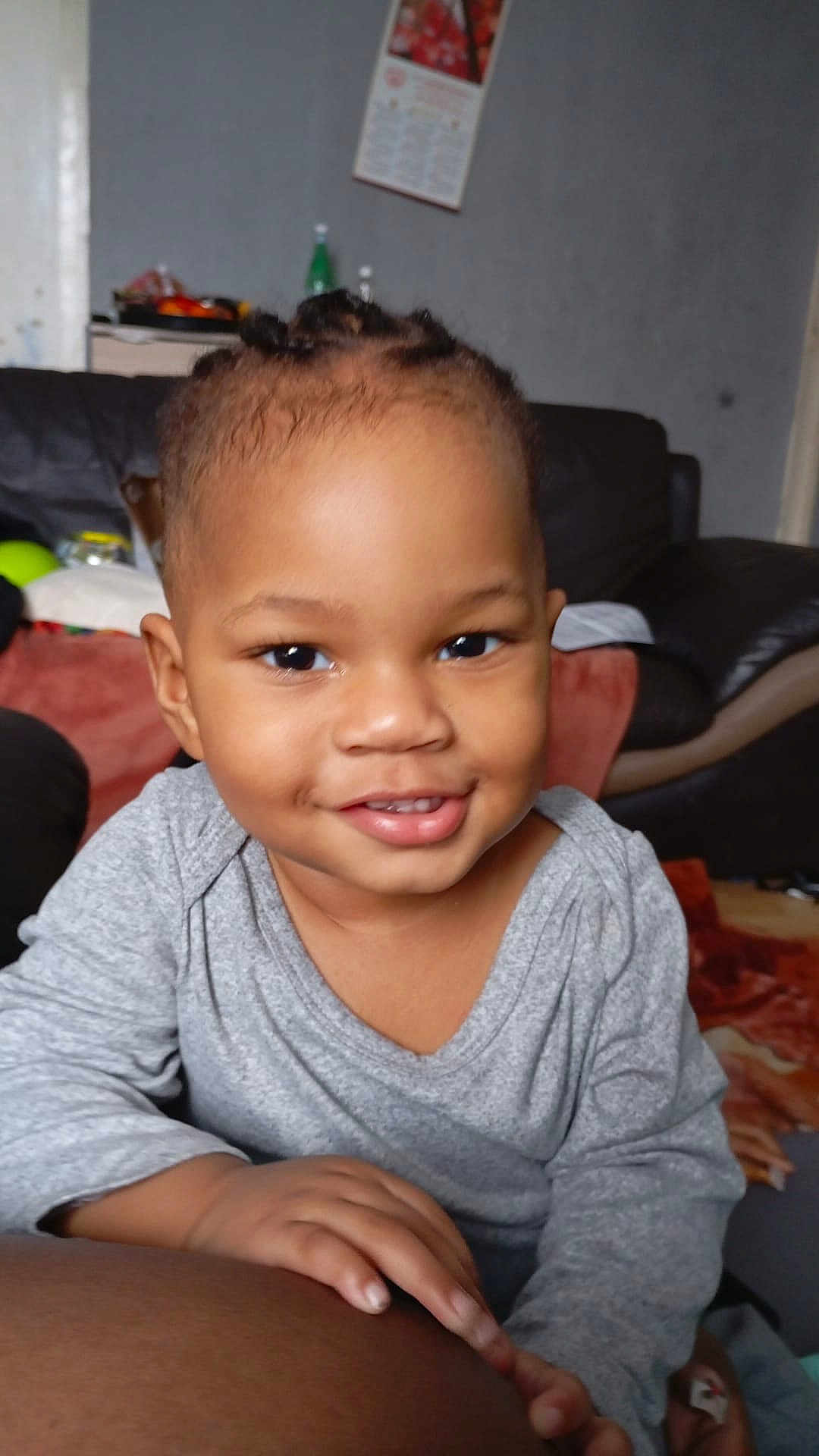 Melyo a rejoint le concours — aidez-le/la à gagner de superbes lots ! toddler, child, smile, face, braids, grey_shirt, hand, indoor, couch, calendar, furniture, room, person, happy, skin, eyes, home, portrait, casual, baby