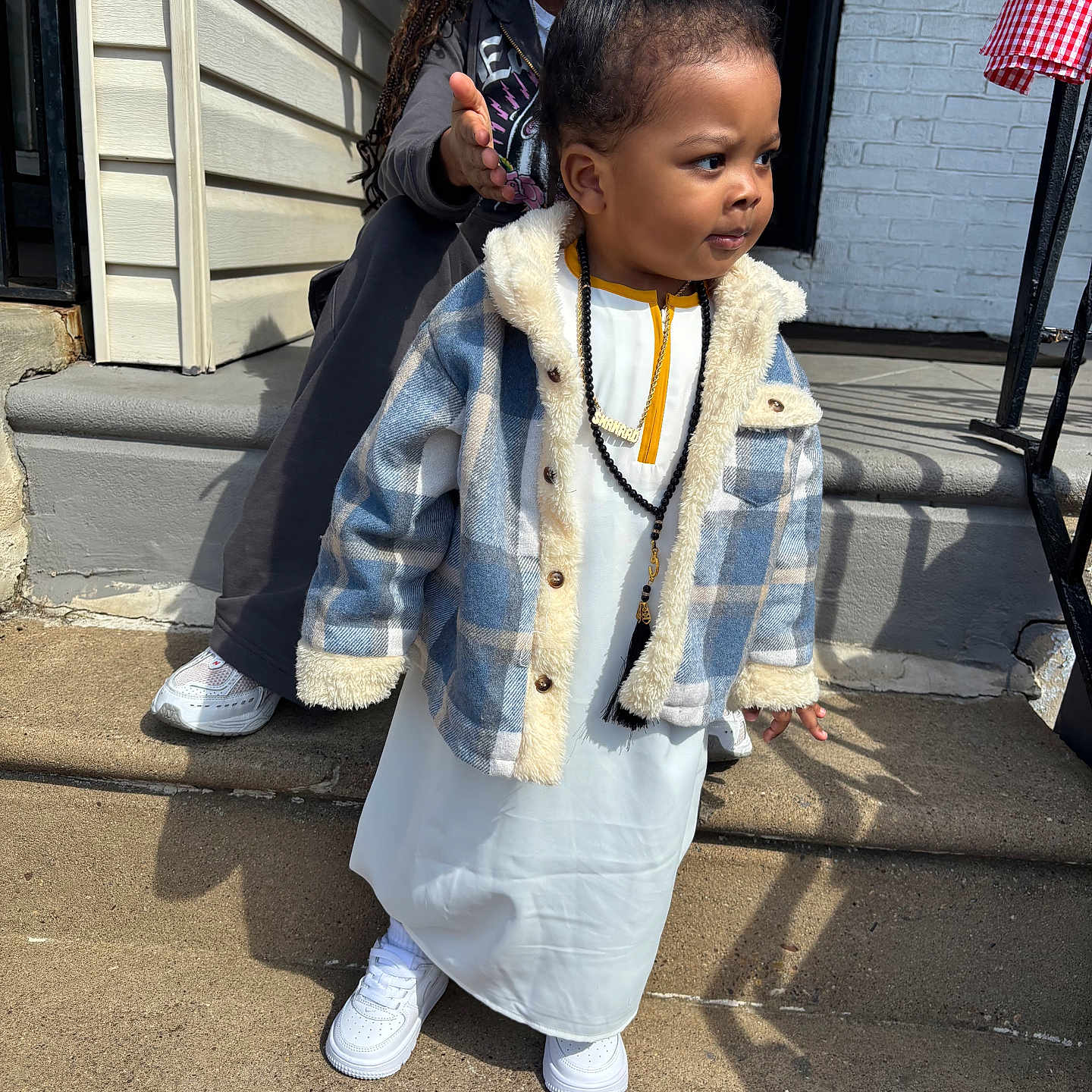 Shahaad is registered to the contest to win money with this photo: child, toddler, woman, braids, jacket, white_outfit, necklace, sneakers, concrete, steps, outdoor, daylight, shadow, hand_gesture, casual_clothing, smiling, person, portrait, street, building