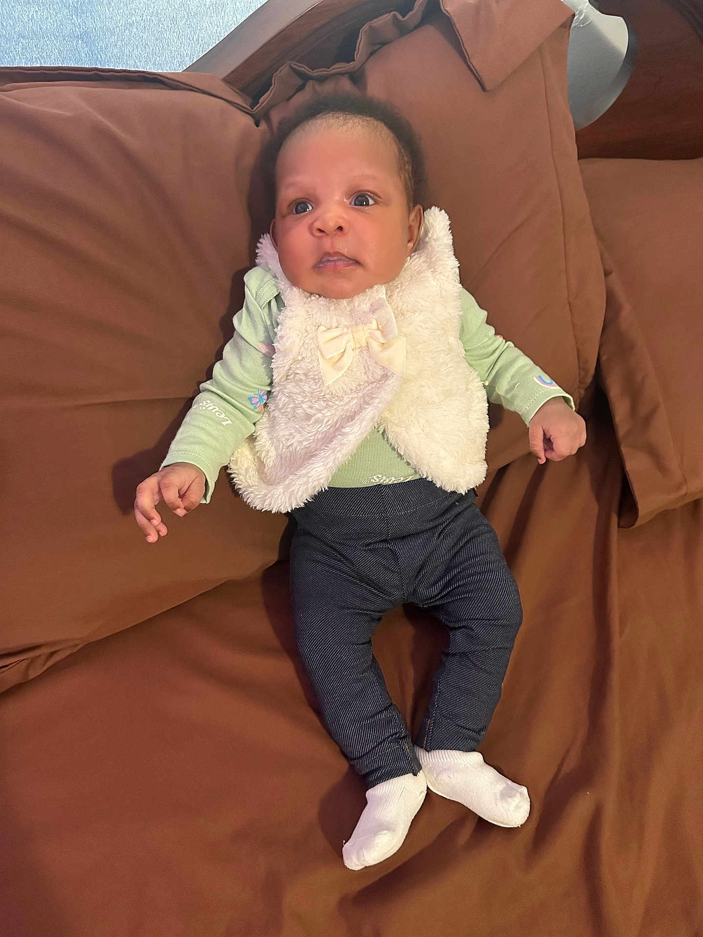 Kierra is registered to the contest to win money with this photo: baby, infant, child, person, clothing, vest, socks, pants, bed, brown_bedspread, lying_down, cute, indoor, young_child, curious, face, hands, feet, sleepwear, portrait