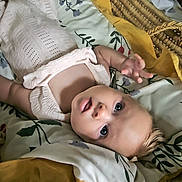 Myra is registered to the contest to win money with this photo: baby, infant, basket, blanket, floral_pattern, mustard_color, sleepwear, lying_down, curious, face, head, skin, hand, indoors, soft_texture, cozy, person, child, newborn, cute