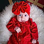baby, infant, red_clothing, headband, bow, fluffy_cushion, gift_box, wide_eyes, surprised_expression, wooden_floor, portrait, indoors, cute, child, soft_texture, buttoned_jacket, holiday_theme, wrapped_presents, sitting, small_hands