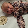 baby, infant, newborn, camo_clothing, plaque, wooden, one_month, quilted_bed, white_background, face, lying_down, portrait, cute, child, young, happy, resting, soft_light, closeup, peaceful