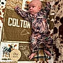 baby, infant, one_month, blanket, cow_pattern, wooden_sign, camouflage_clothing, lying_down, newborn, feet, hand, face, head, plaid, animal_print, soft_texture, cute, milestone, portrait, indoor