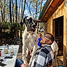 Atlas participe au concours pour gagner de l'argent avec cette photo : dog, great_dane, man, person, outdoor, wooden_cabin, table, drink, glass, forest, trees, sunny, smile, chair, casual, relaxing, daylight, nature, happy, plaid_jacket