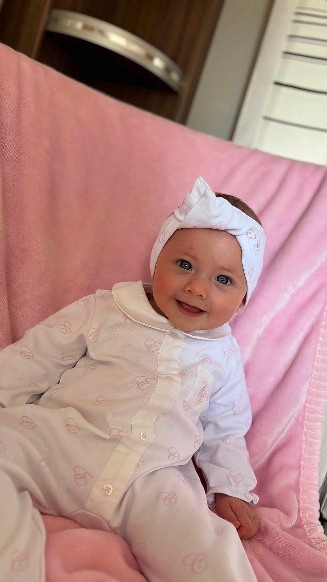 Djynn a rejoint le concours — aidez-le/la à gagner de superbes lots ! baby, child, smiling, onesie, headband, pink_blanket, indoor, cute, portrait, happy, infant, clothing, face, person, sitting, soft_texture, cozy, baby_girl, closeup, comfortable