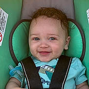 Josiah is registered to the contest to win money with this photo: baby, child, car_seat, smiling, pacifier, blue_shirt, curly_hair, infant, safety_harness, seat_belt, cute, portrait, indoors, person, young_child, happy, close_up, seat, child_safety, toddler
