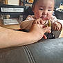 toddler, child, hand, green_beans, indoor, curious, person, furniture, high_chair, clothing, face, skin, short_hair, food, kitchen, background, table, leather, interaction, focus
