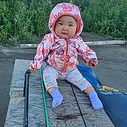 Tabitha joined the competition — help win amazing prizes! baby, child, hooded_jacket, floral_pants, purple_socks, outdoor, wooden_surface, greenery, nature, cute, seated, smiling, face, person, baby_clothing, cold_weather, park, dirt_ground, daylight, casual