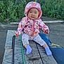 baby, child, hooded_jacket, floral_pants, purple_socks, outdoor, wooden_surface, greenery, nature, cute, seated, smiling, face, person, baby_clothing, cold_weather, park, dirt_ground, daylight, casual