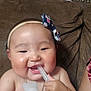 Tabitha joined the competition — help win amazing prizes! baby, child, headband, smiling, chewing, plastic_tube, couch, brown, floral_pattern, indoor, person, skin, hand, face, cheek, happy, infant, cute, closeup, expression