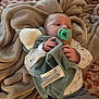 baby, pacifier, blanket, plush_toy, bedspread, infant, clothing, striped_pants, patterned_shirt, soft_texture, bedroom, sleeping_area, comfort, cute, hand, face, head, lying_down, resting, warm