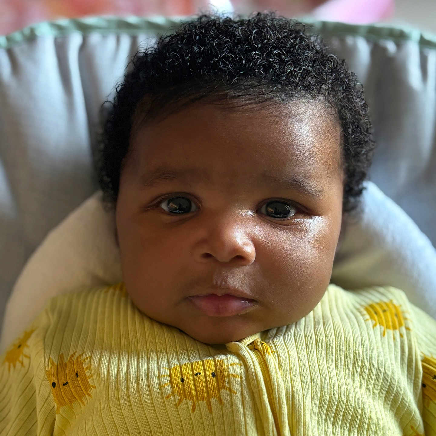 Nahée a rejoint le concours — aidez-le/la à gagner de superbes lots ! apparel, baby, child, close_up, cozy, curly_hair, cute, expression, face, head, indoors, infant, newborn, person, portrait, sitting, soft_background, sun_pattern, yellow_clothing, young_child