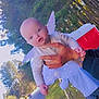 baby, angel_wings, sparkles, outdoor, trees, road, person, hand, tattoo, costume, white_clothing, grass, daylight, nature, holding, child, cute, portrait, smile, toddler