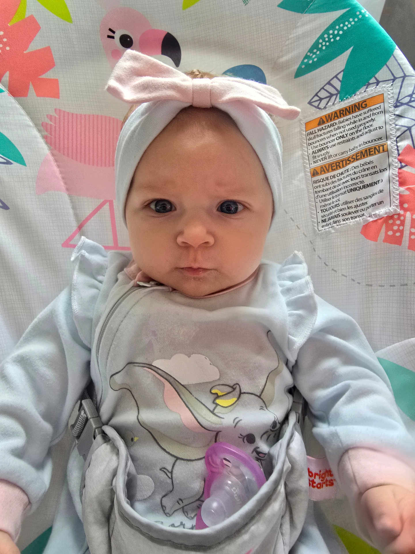 Raelynn is registered to the contest to win money with this photo: baby, infant, headband, pink_bow, pacifier, onesie, dumbo, elephant, seat, baby_seat, flamingo, pattern, colorful, clothing, face, expression, indoor, child, cute, portrait