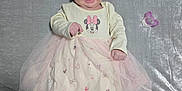 Raelynn is registered to the contest to win money with this photo: baby, infant, smiling, lying_down, dress, minnie_mouse, pink, pacifier, blanket, soft_texture, cute, happy, child, footwear, toddler, clothing, person, indoors, head, face