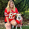 woman, person, dog, pet, outdoor, garden, grass, greenery, portrait, smiling, kneeling, football_jersey, sports, team, red_clothing, matching_outfits, collar, shorts, nature, photography
