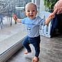baby, child, indoor, walking, support, hand, blue_shirt, cartoon_bear, pants, barefoot, floor, glass_door, window, smudged_window, smile, happy, person, toddler, home, plant