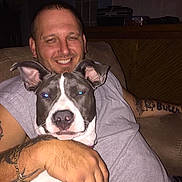 Jasmine joined the competition — help win amazing prizes! man, dog, indoor, couch, smiling, tattoos, bracelet, short_sleeves, flash, blue_eyes, pet, hugging, furniture, home, relaxed, portrait, seated, living_room, person, animal