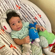 Ryan Christopher is registered to the contest to win money with this photo: baby, infant, child, portrait, lying_down, smiling, awake, face, dark_hair, onesie, clothing, blanket, cushion, baby_seat, stuffed_animal, plush_toy, bedroom, indoor, cozy, photograph