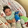 baby, infant, child, portrait, lying_down, smiling, awake, face, dark_hair, onesie, clothing, blanket, cushion, baby_seat, stuffed_animal, plush_toy, bedroom, indoor, cozy, photograph