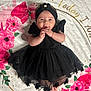 baby, black_dress, headband, flower, blanket, floral_pattern, pink_flowers, red_flowers, infant, cute, happy, lying_down, hands, feet, soft_texture, portrait, child, adorable, smiling, indoor