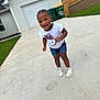 toddler, child, smiling, braided_hair, white_tshirt, hello_kitty, denim_shorts, white_sneakers, driveway, concrete, house, garage, green_trash_bins, outdoor, daylight, happy, person, casual_clothing, suburban, playful