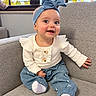 Leah is registered to the contest to win money with this photo: baby, child, infant, smiling, happy, portrait, sitting, couch, indoor, window, sunlight, headband, bow, blue_clothing, white_shirt, floral_pants, socks, furniture, home, face
