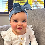 Leah joined the competition — help win amazing prizes! baby, child, infant, smiling, portrait, indoors, chair, couch, blue_bow, headband, white_sweater, ruffles, buttons, skirt, window, blinds, sunlight, brown_hair, happy, sitting