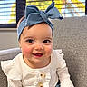 baby, child, infant, smiling, portrait, indoors, chair, couch, blue_bow, headband, white_sweater, ruffles, buttons, skirt, window, blinds, sunlight, brown_hair, happy, sitting