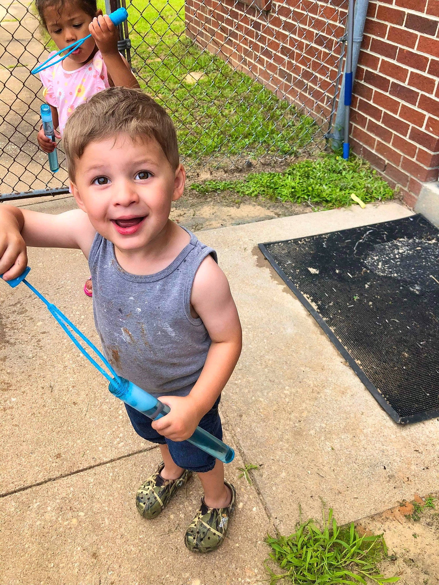 Clayton is registered to the contest to win money with this photo: child, fence, flip_flops, fun, grass, grass_family, green, happy, head, joy, lawn, leg, leisure, people_in_nature, person, recreation, sandal, shorts, sidewalk, smile