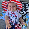 baby, child, smiling, hat, red_white_blue, stars_and_stripes, outdoor, blanket, concrete, shoes, celebration, holiday, clothing, person, infant, cute, patriotic, red_beads, happy, lying_down