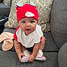 Ariyah joined the competition — help win amazing prizes! baby, child, infant, portrait, sitting, couch, sofa, hat, football_hat, sportswear, red_clothing, white_bib, sneakers, shoes, smiling, indoors, living_room, cushions, happy, cute