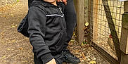 Ajay joined the competition — help win amazing prizes! toddler, child, black_tracksuit, outdoor, path, dirt, leaves, fence, adult, hand, curious, smile, short_hair, sneakers, nature, trees, wooden_fence, daylight, person, playful