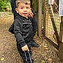 toddler, child, black_tracksuit, outdoor, path, dirt, leaves, fence, adult, hand, curious, smile, short_hair, sneakers, nature, trees, wooden_fence, daylight, person, playful