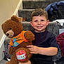 child, boy, smile, teddy_bear, birthday, stairs, carpet, clothing, indoor, home, happy, toy, person, casual, shorts, shirt, earring, footwear, background, celebration
