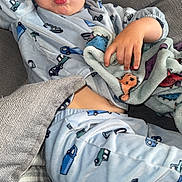 Ajay is registered to the contest to win money with this photo: child, pajamas, blue, car_pattern, face, hand, blanket, couch, cushion, expression, playful, indoors, relaxing, person, smile, funny_face, cozy, toddler, home, casual