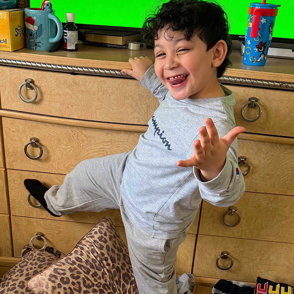 Mesiah is registered to the contest to win money with this photo: animated_show, carpet, casual, child, cup, curly_hair, dresser, furniture, gray_clothing, happy, indoor, leopard_print, person, pillows, playful, smiling, socks, television, tongue_out, toy