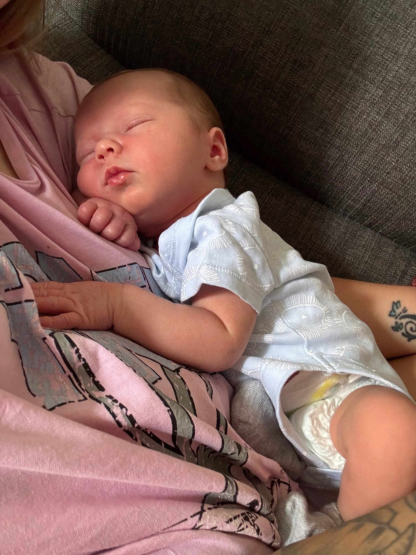 Leo is registered to the contest to win money with this photo: newborn, baby, sleeping, infant, person, pink_shirt, couch, arm, tattoo, diaper, white_clothing, relaxation, closeup, indoor, comfort, peaceful, skin, human, portrait, rest