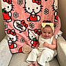 baby, child, infant, smile, headband, knitwear, white_clothing, chair, blanket, hello_kitty, pink, pattern, flower, apple, wooden_sign, months, indoor, cute, milestone, happy