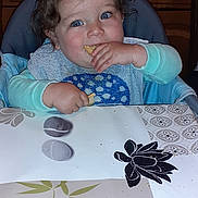 Noah a rejoint le concours — aidez-le/la à gagner de superbes lots ! toddler, child, high_chair, snack, blue_eyes, curly_hair, kitchen, table, bib, eating, food, countertop, stove, utensils, plate, person, indoor, happy, cute, baby