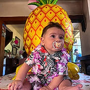 Aylhan a rejoint le concours — aidez-le/la à gagner de superbes lots ! baby, celebration, child, colorful, cute, decorations, face, floral_shirt, flower_garland, indoor, infant, pacifier, party, person, pineapple_balloon, sitting, skin, smiling, table, toddler