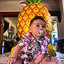 baby, celebration, child, colorful, cute, decorations, face, floral_shirt, flower_garland, indoor, infant, pacifier, party, person, pineapple_balloon, sitting, skin, smiling, table, toddler