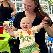 Kaleb is registered to the contest to win money with this photo: baby, child, infant, smiling, happy, portrait, adults, family, outdoor, backyard, party, picnic, balloons, colorful_clothing, green_shorts, black_shirt, woman, holding, seated, sunlight